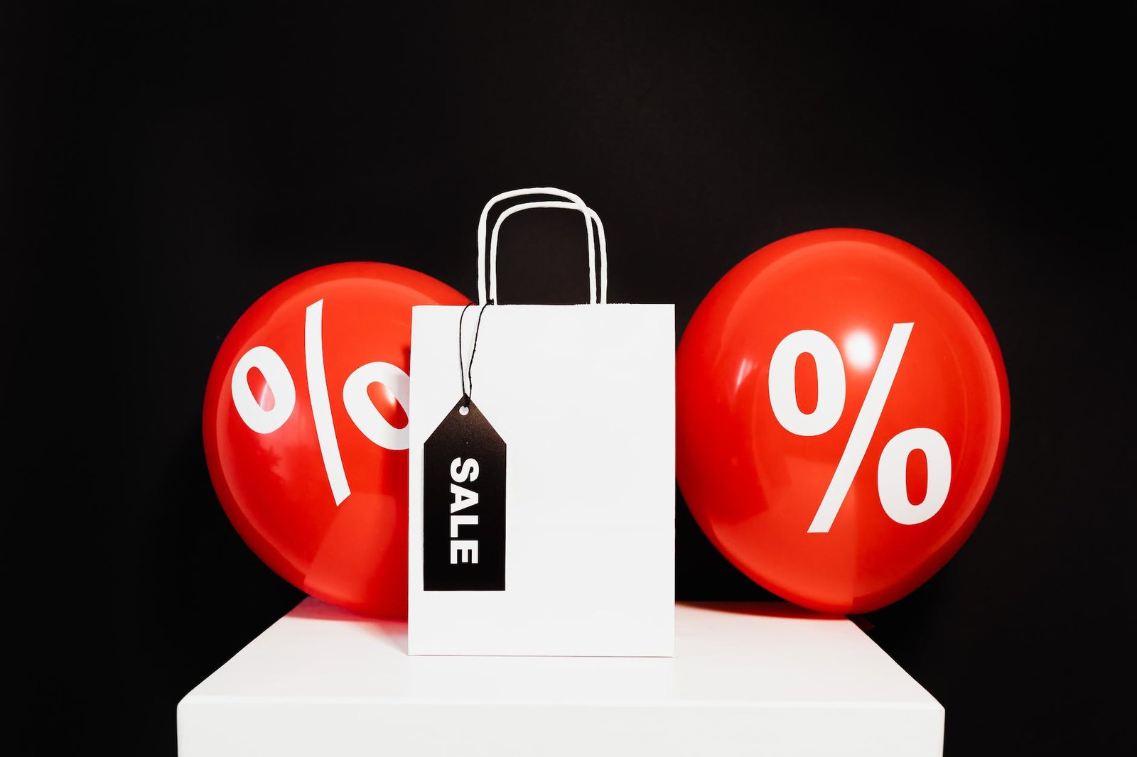 a white Digital marketing paper bag in between red balloons with percentage symbol on a black background